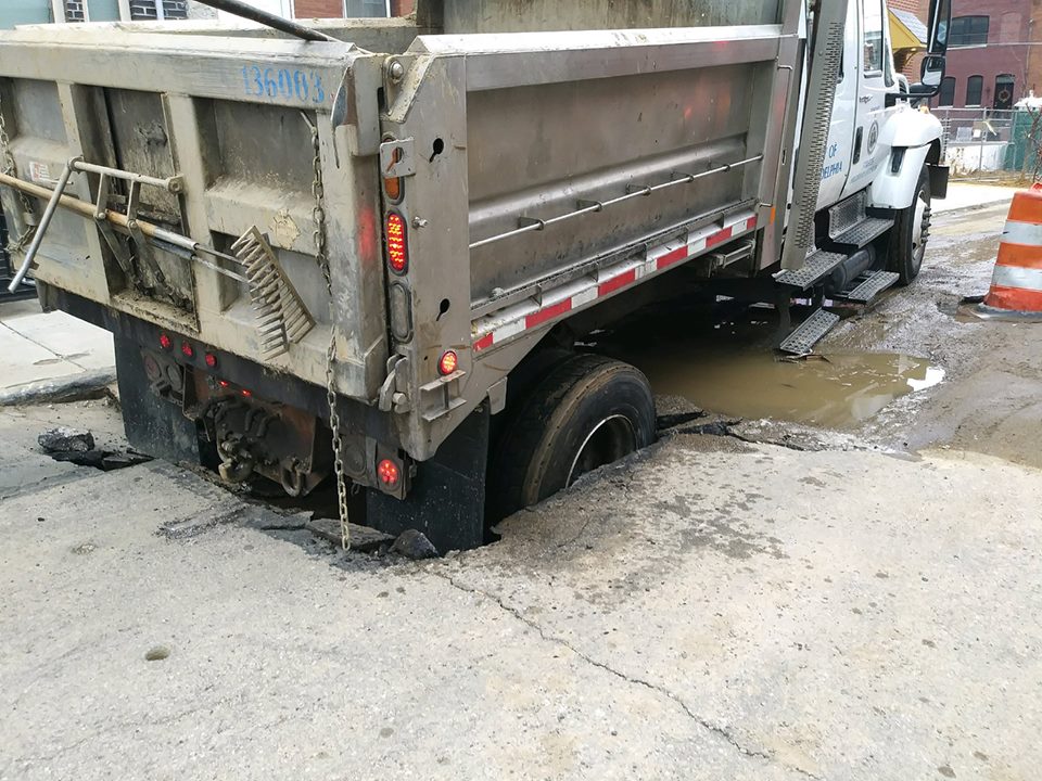 Dump truck on the street, whose read wheel has fallen into a sinkhole